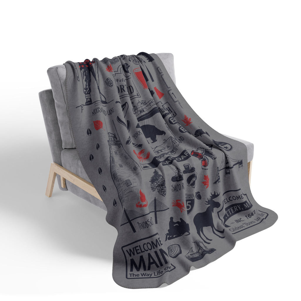 Gray Maine landmark and wildlife collage blanket with red accents draped over a chair