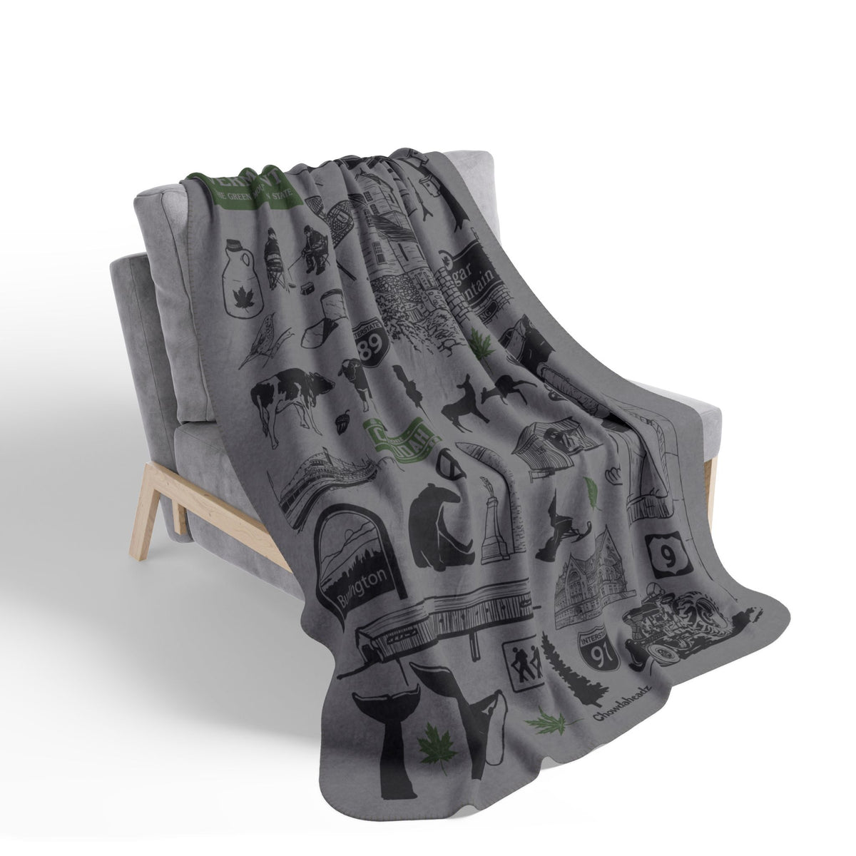 Gray Vermont landmark and wildlife collage blanket with green accents draped over a chair