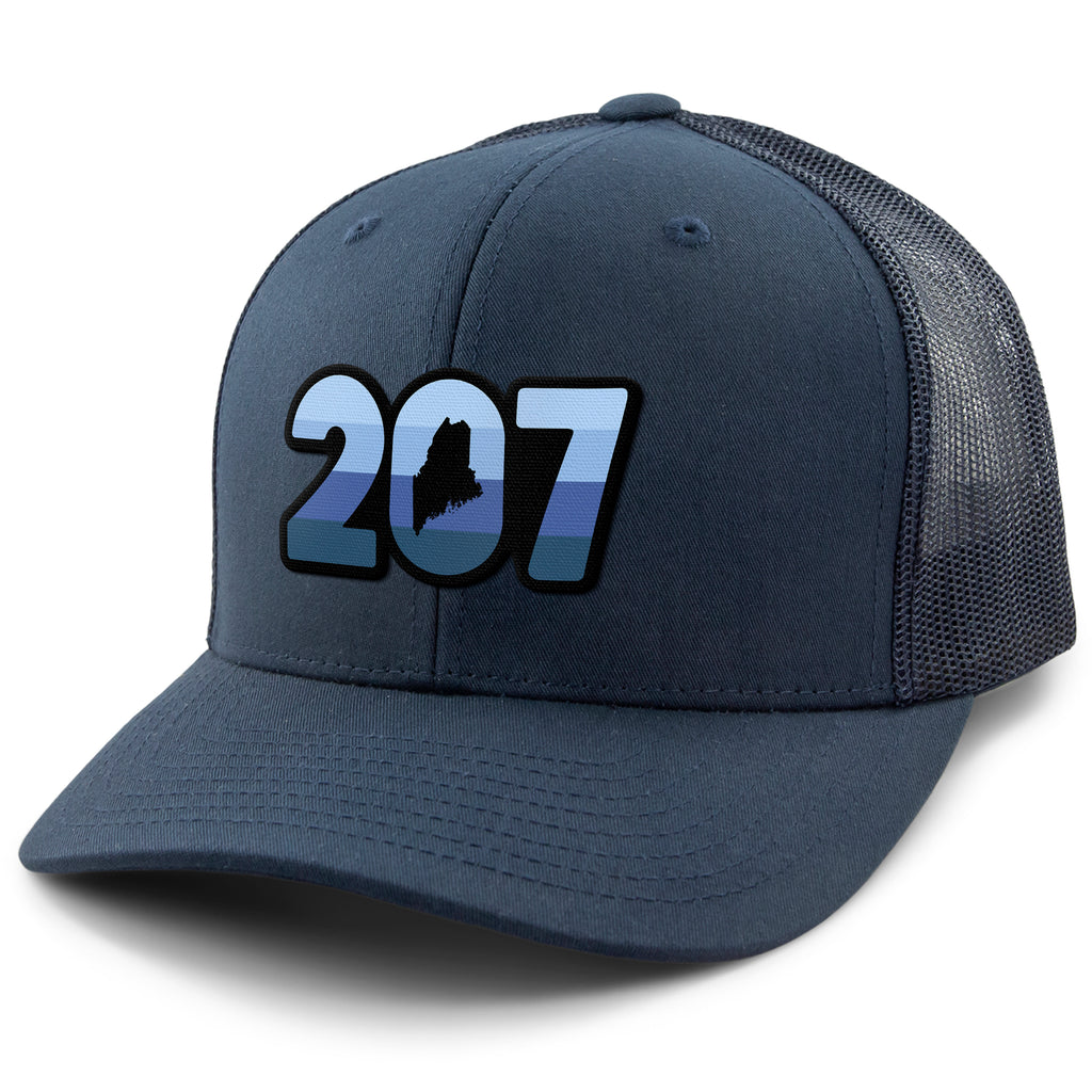Three-quarter front view of a navy Retro 207 Maine snapback trucker hat with blue-striped numbers and a state silhouette in the zero