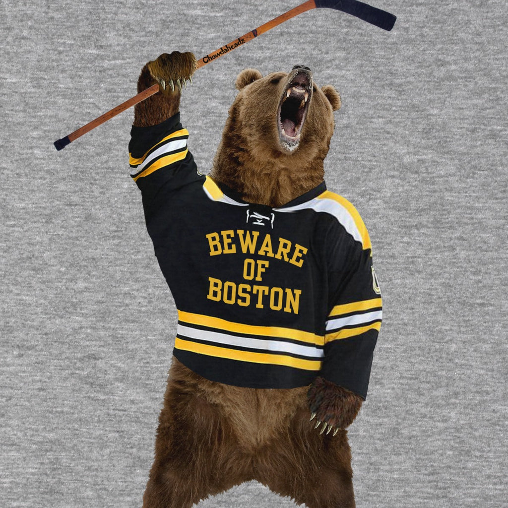 Close-up of the “Beware of Boston” bear in a black, gold and white hockey jersey holding a stick overhead on gray fabric