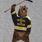 Close-up of the “Beware of Boston” bear in a black, gold and white hockey jersey holding a stick overhead on gray fabric